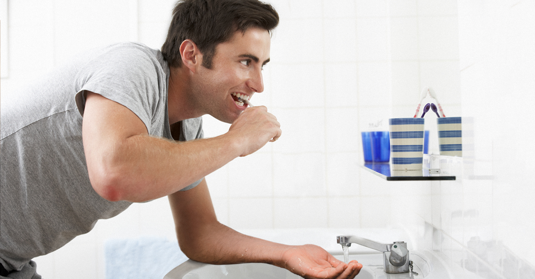 صورة شاب يمتنع عن الإسراف بالماء ويضع يده أسفل الصنبور أثناء تنظيف أسنانه